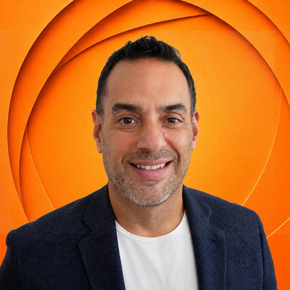 Frank Mesa smiling, wearing a navy blazer and white shirt against a sculpted orange background.